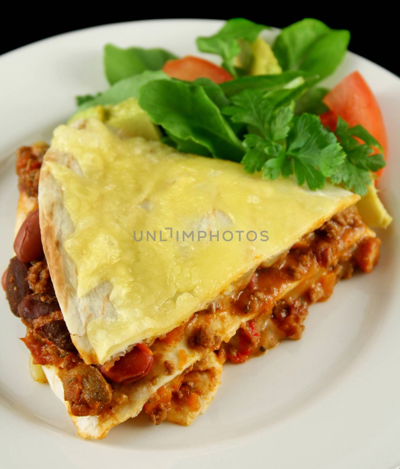 A slice of beef and bean Mexican tortilla stack with cheese and salad.