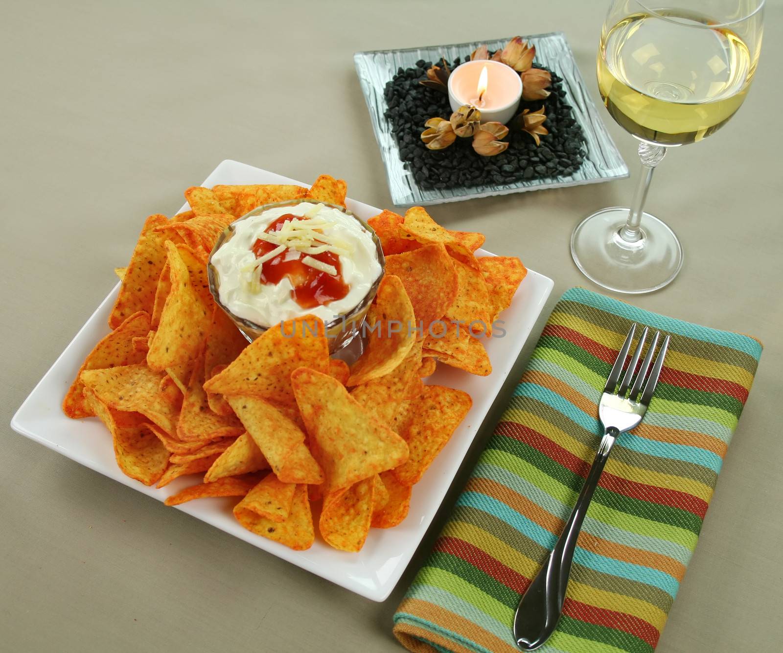 Nachos and Mexican dip topped with sour cream, salsa and grated cheese with copy space top left.