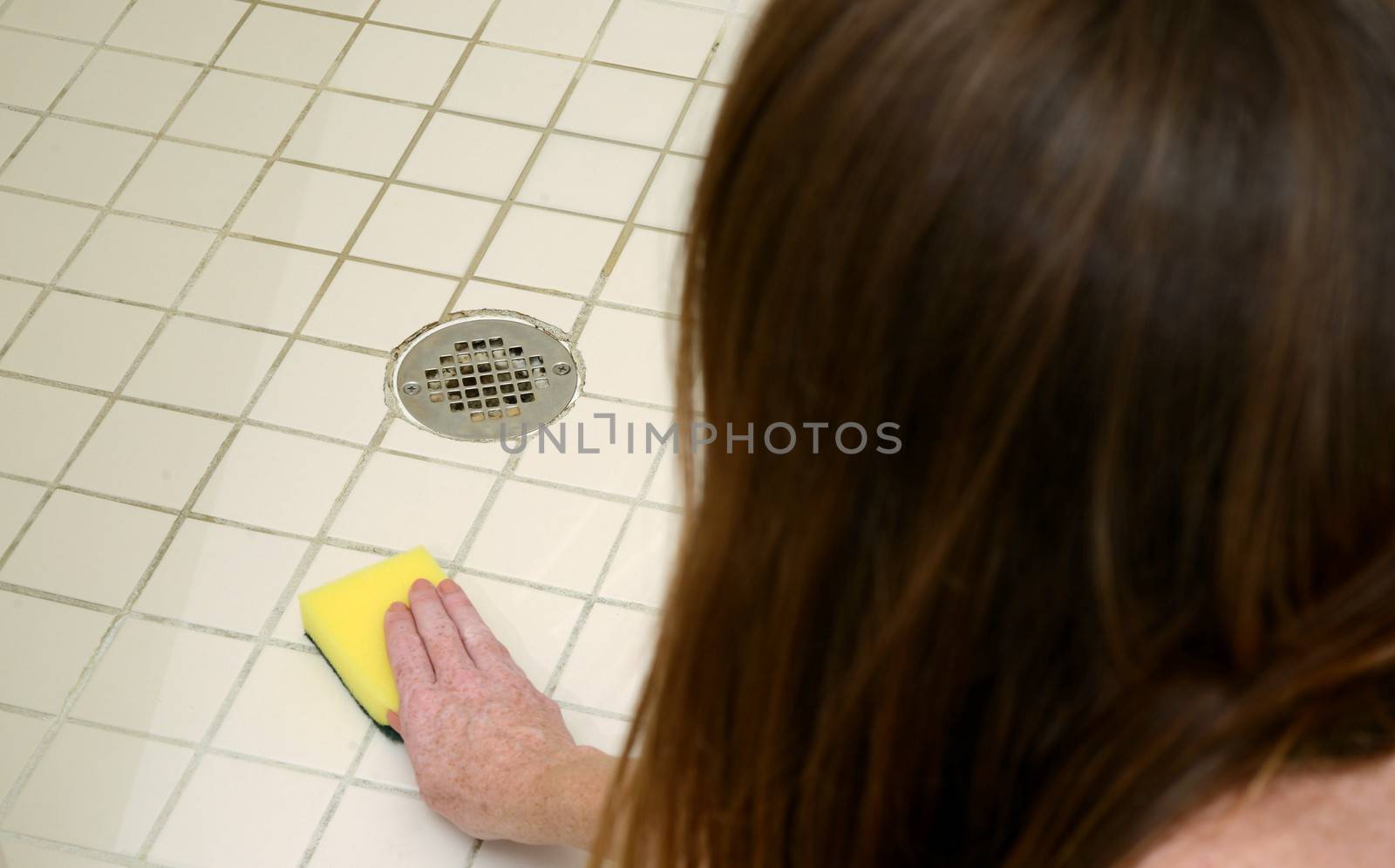 woman scrubbing shower tiles with scour pad to clean soap scum