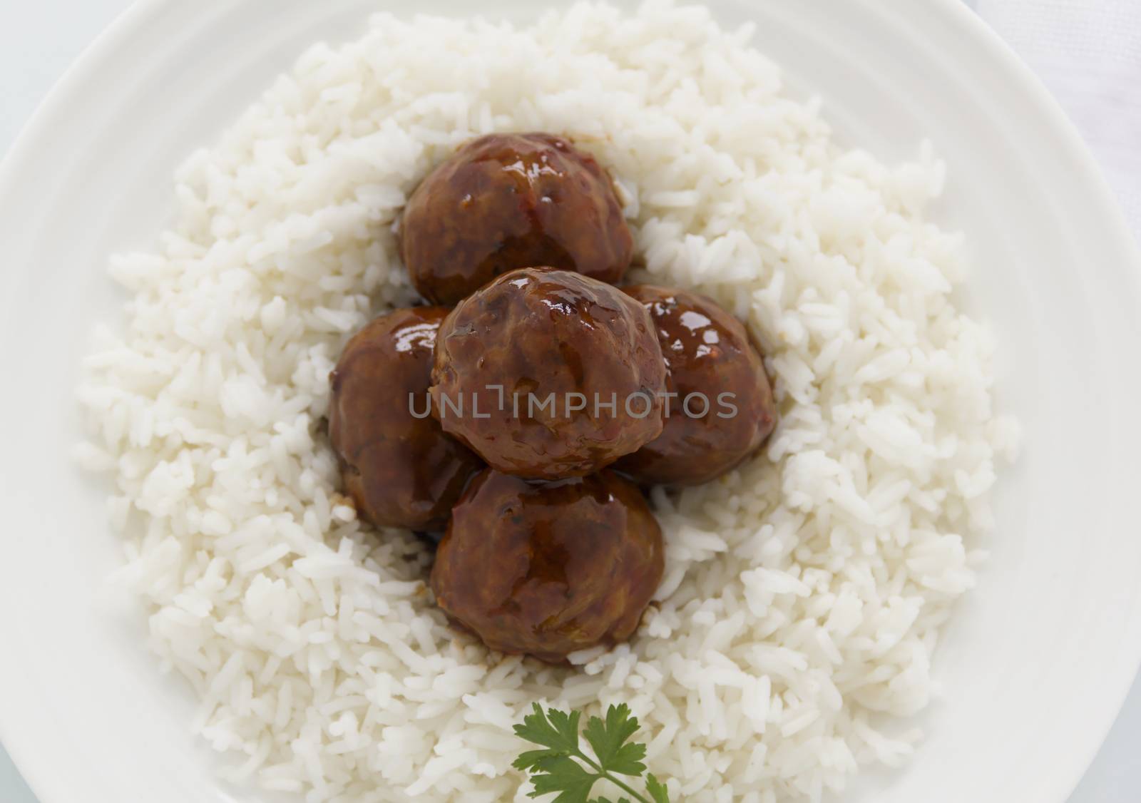 Chinese meat balls in hoisin sauce on a bed of white rice with parsley.