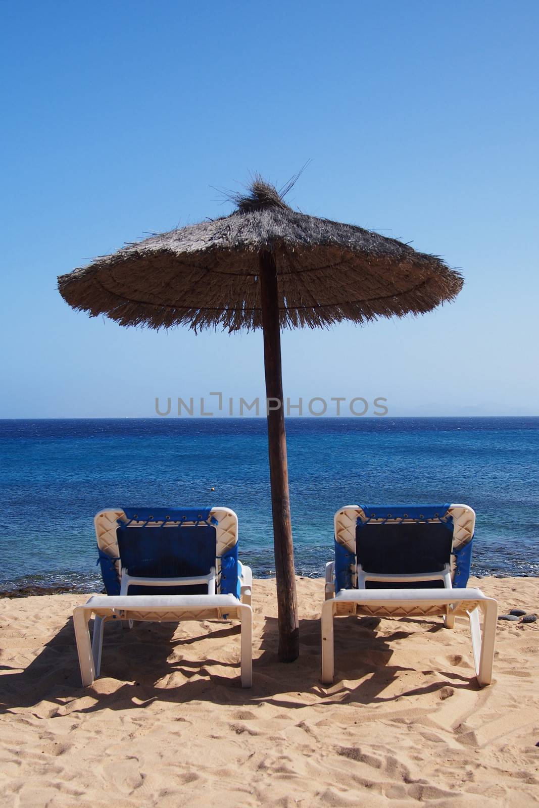 Sunchairs under an umbrella at tropical beach by stockyimages