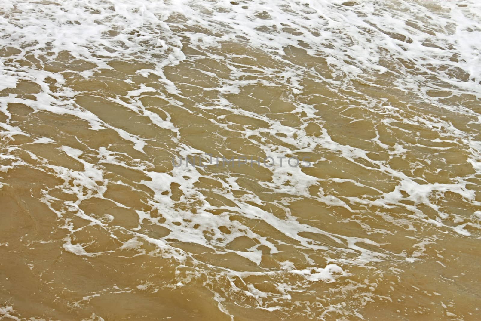 Coastal foamy seawater surface after the storm polluted dredged from the seabed sand