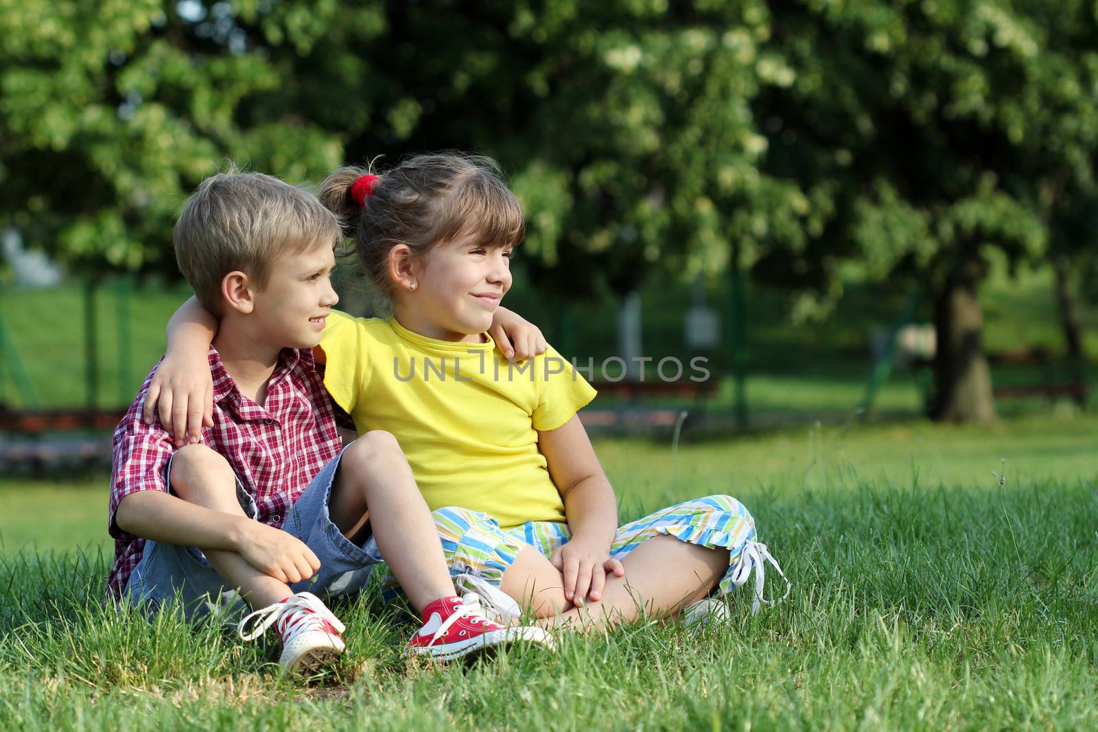 boy and little girl sitting on grass in park by goce