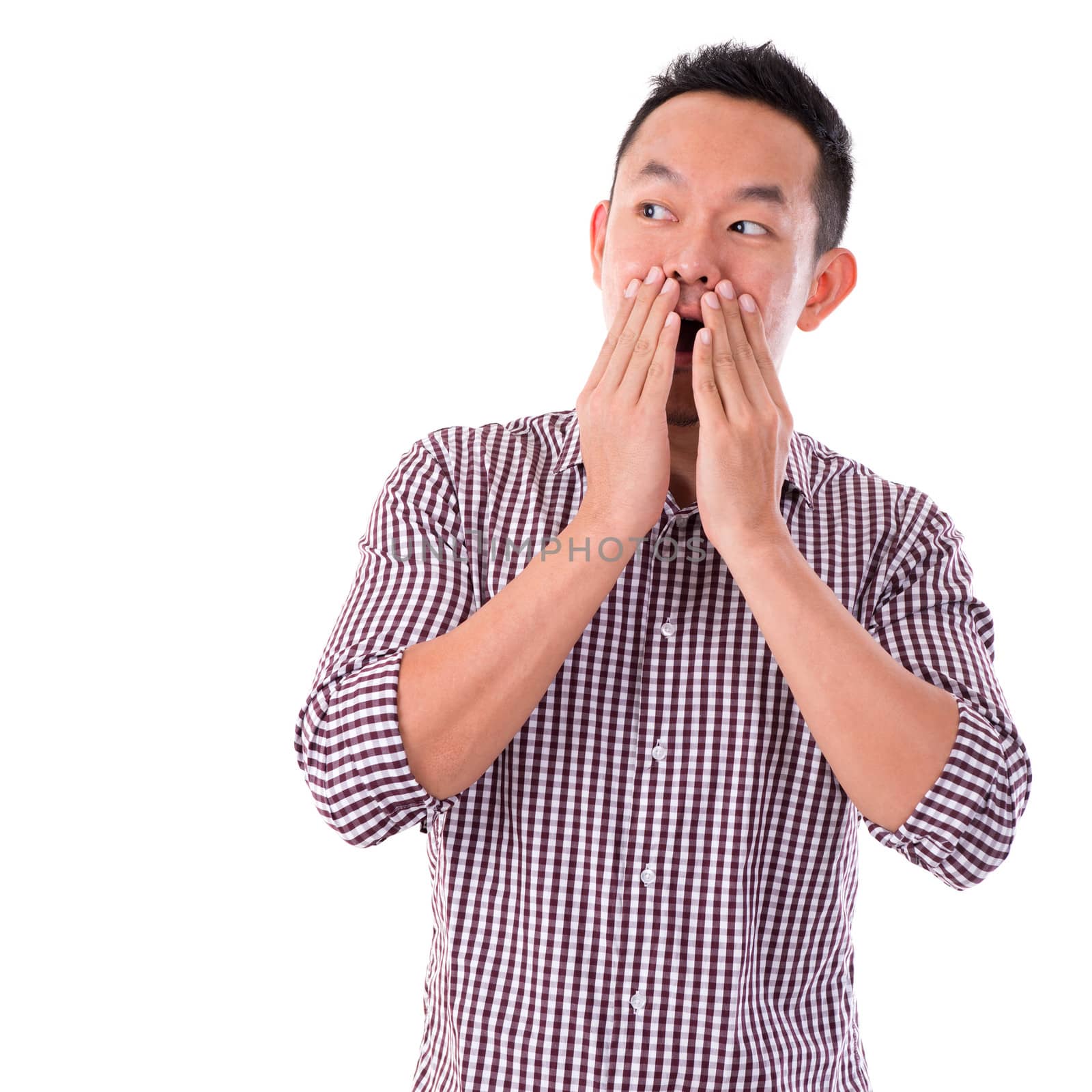 Shocked Asian man covering his mouth by hand, isolated on white background. Asian male model.