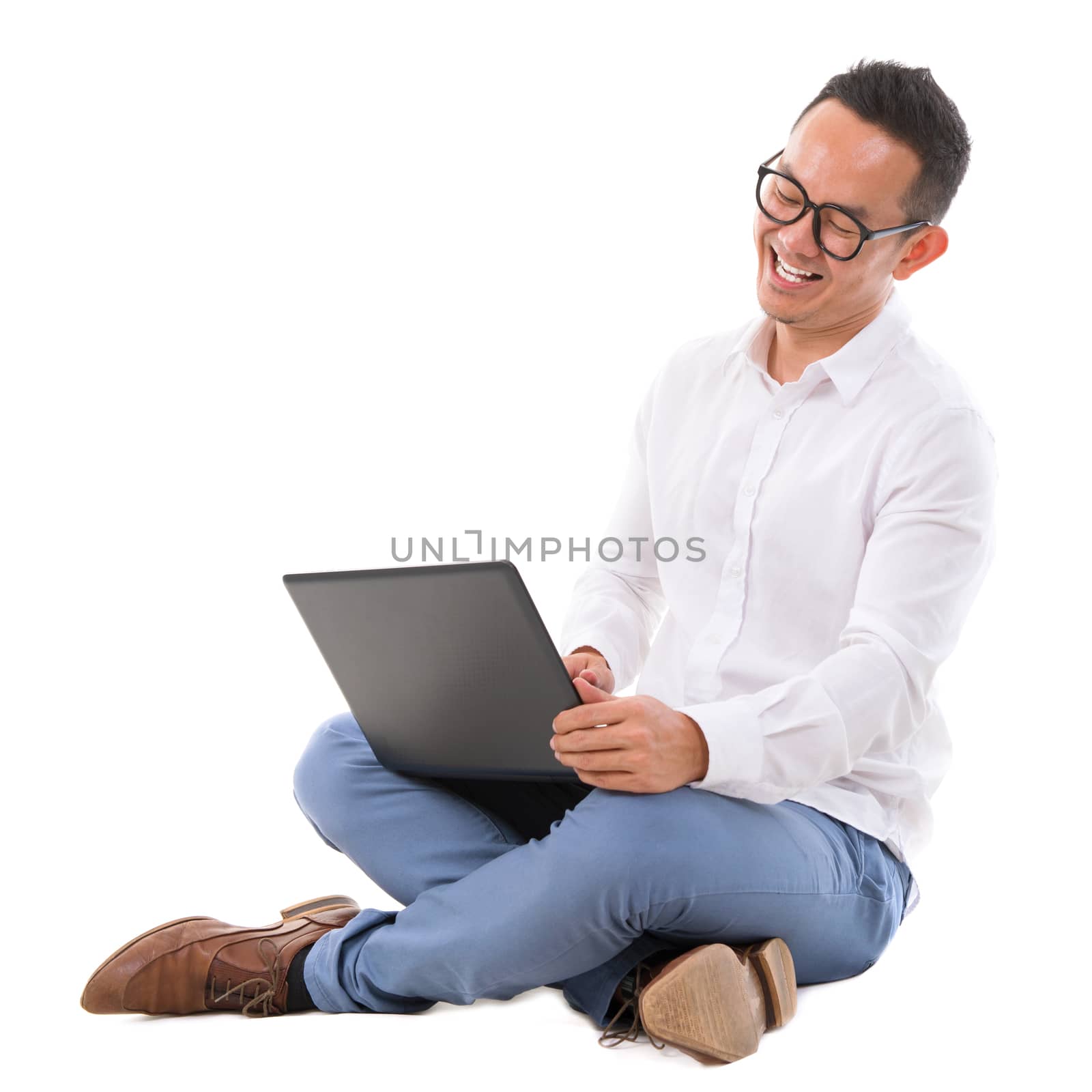Full length of excited Asian businessman looking at laptop sitting over  white background