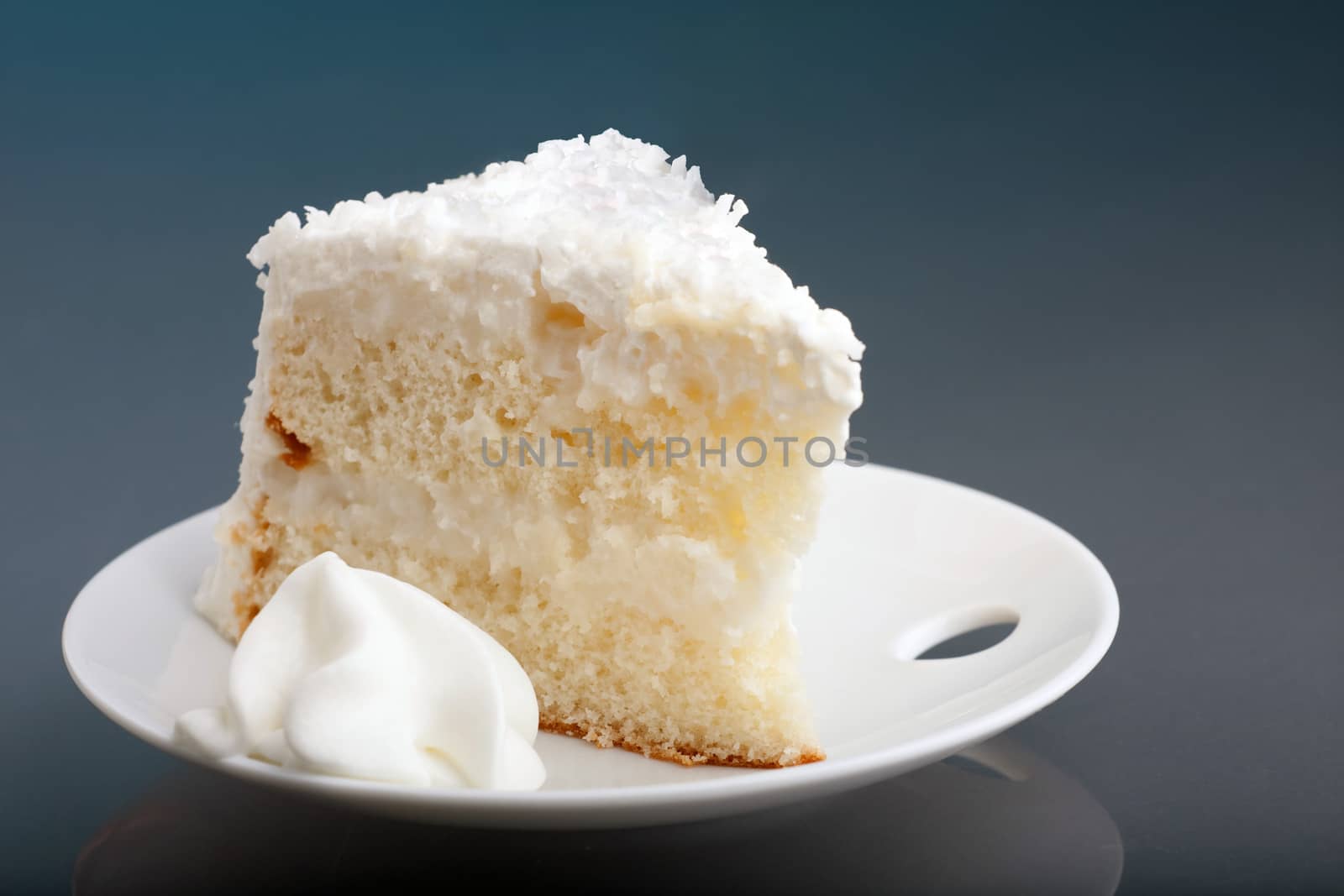 A fresh piece of coconut cream cake on a white plate with a bit of whipped cream on the side.