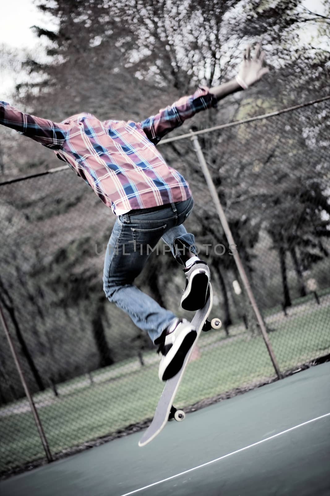 A skateboarder performs tricks in some tennis courts.