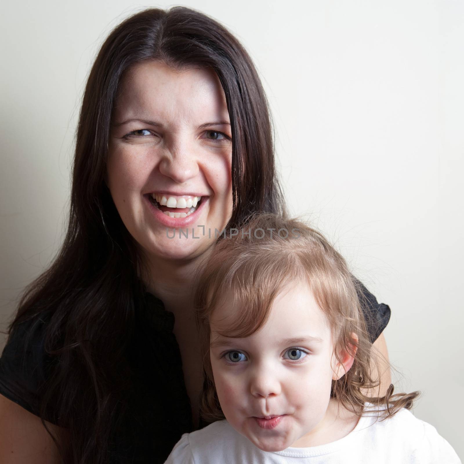 Toddler age girl sitting with her smiling mother while making funny monkey faces.