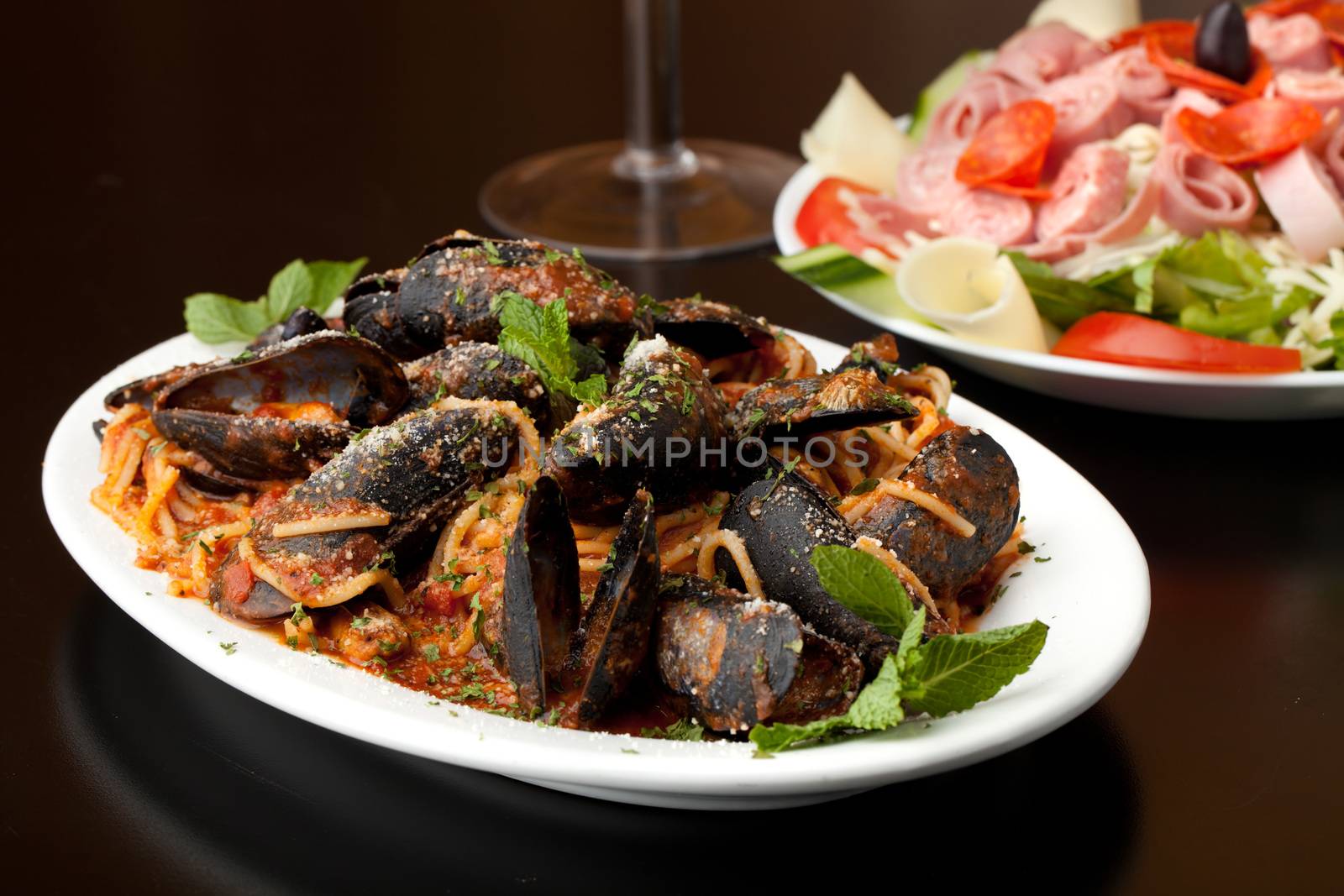 Mussels dinner with red sauce and pasta and an antipasto salad.  Shallow depth of field.