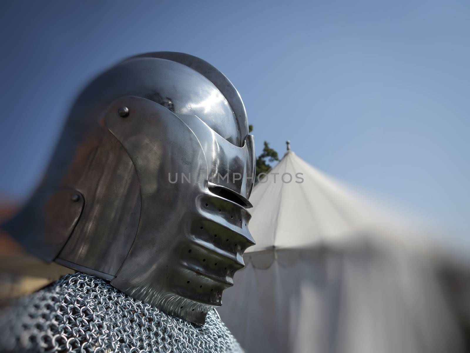 Knight in coat of mail and helmet in front of his tent ready for a fight.