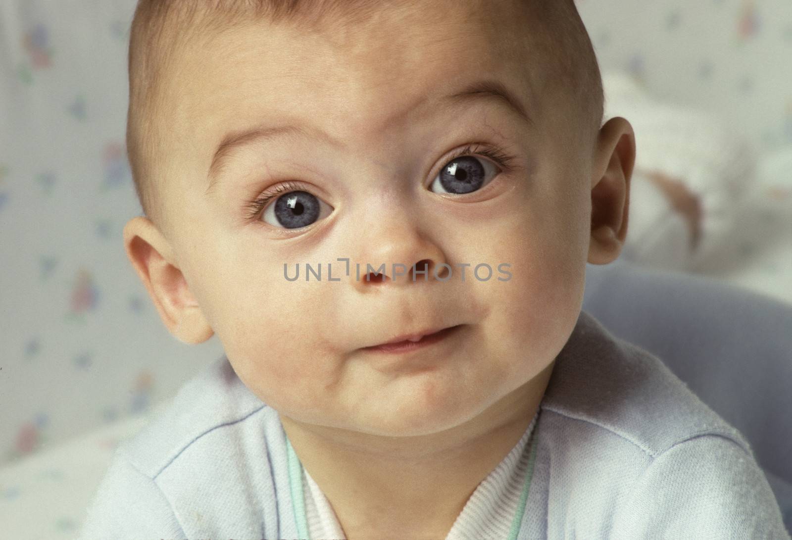 Baby with wide eyes looking directly to camera with an inquistive expression