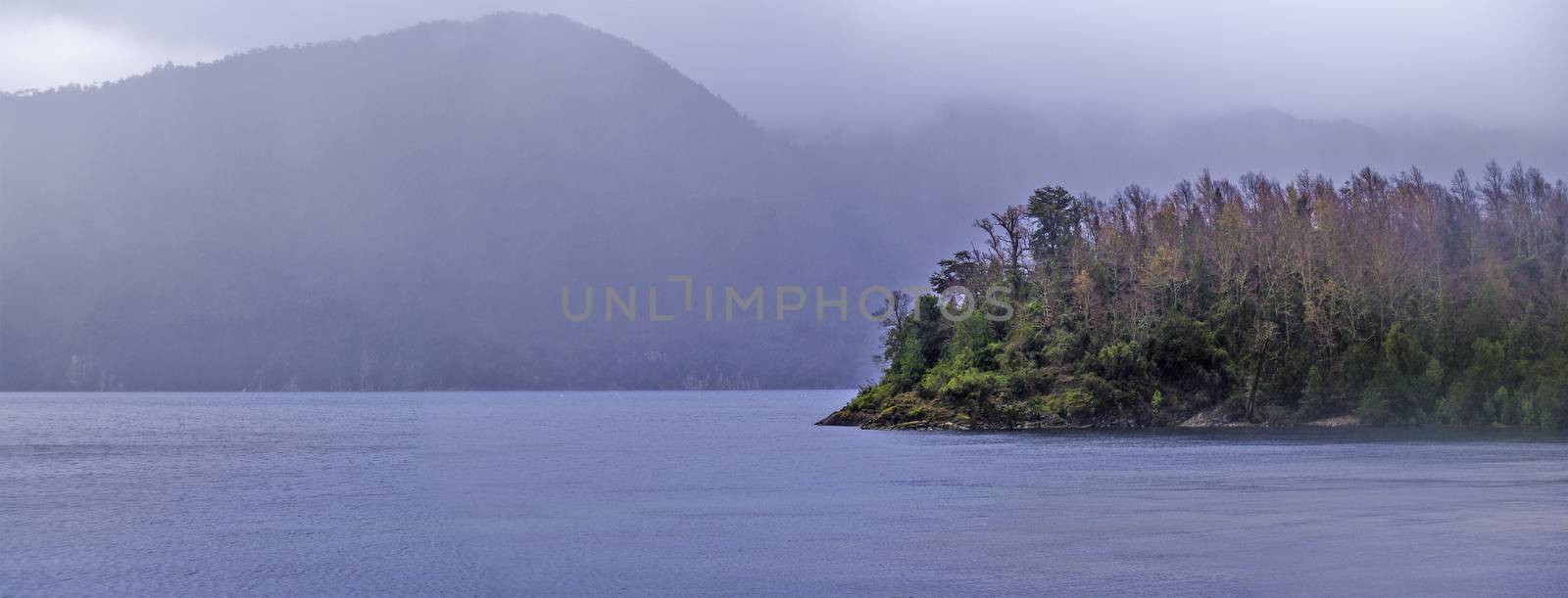 Panorama view of a lake with forest and mountains in the fog