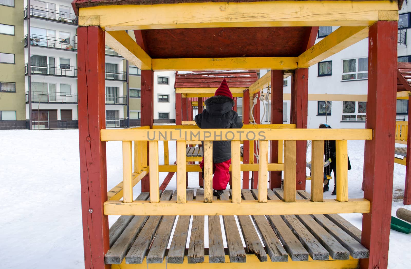 little girl with a gray jacket standing in a wooden hut decorated with yellow of a rail