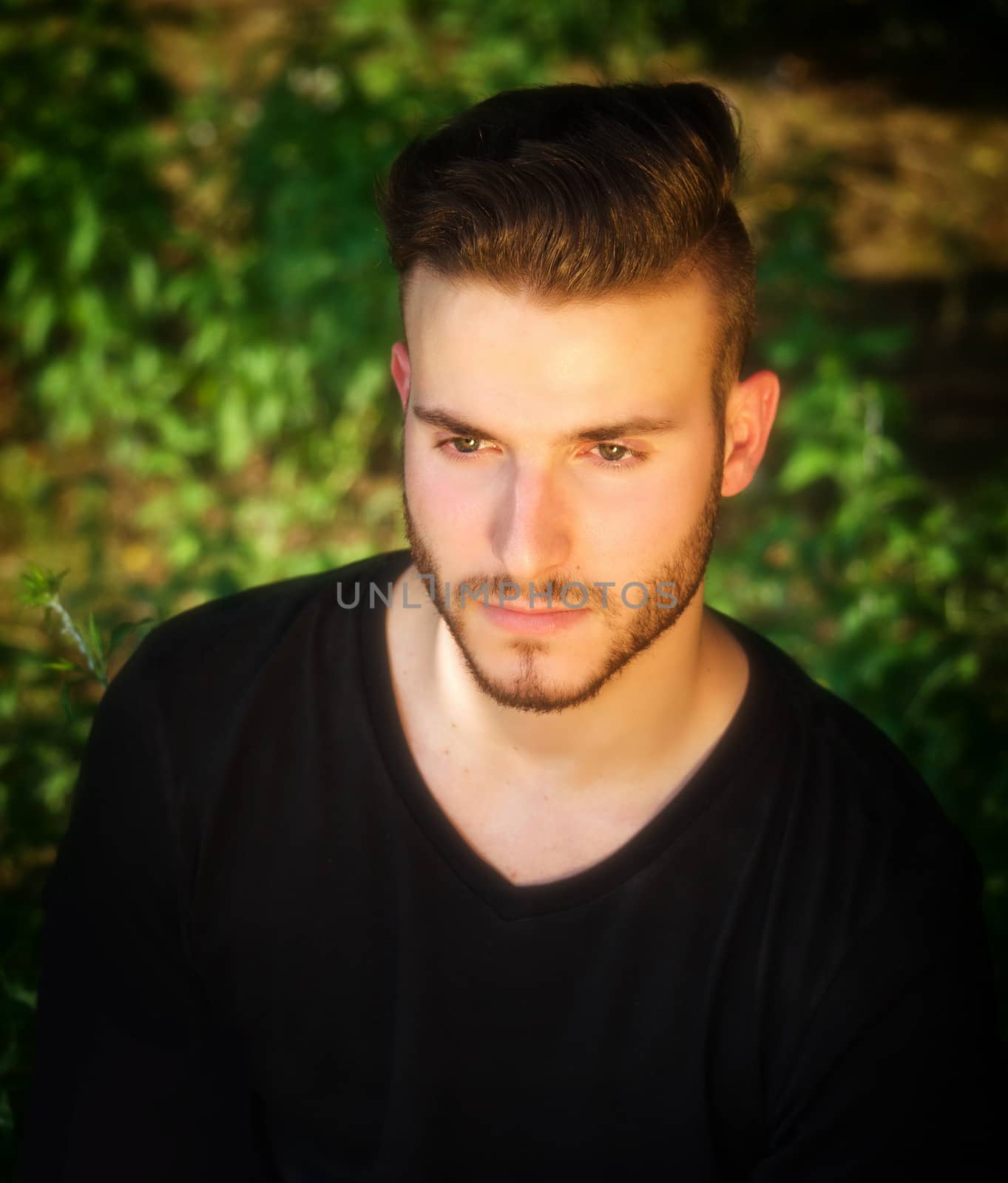 Attractive young man outside, with black t-shirt, serious expression looking off camera