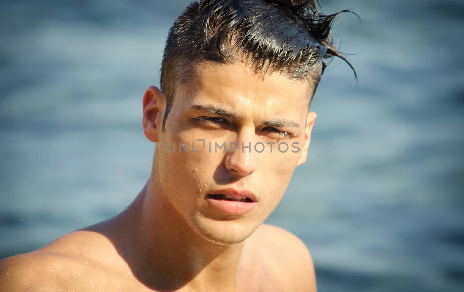 Attractive young man in the sea getting out of water with wet hair, looking in camera