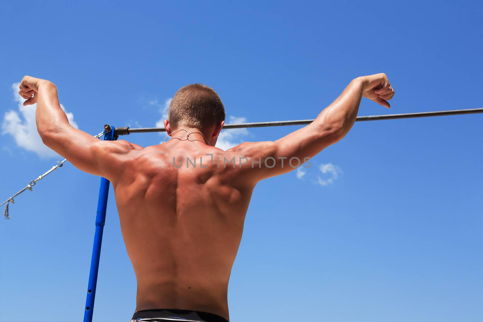 Young strong athlete standing before horizontal bar against blue sky