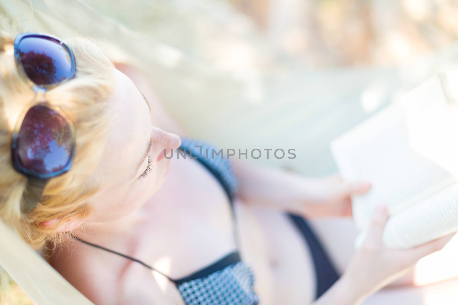 Beautiful girl lies on hammock on the beach and reads the book.