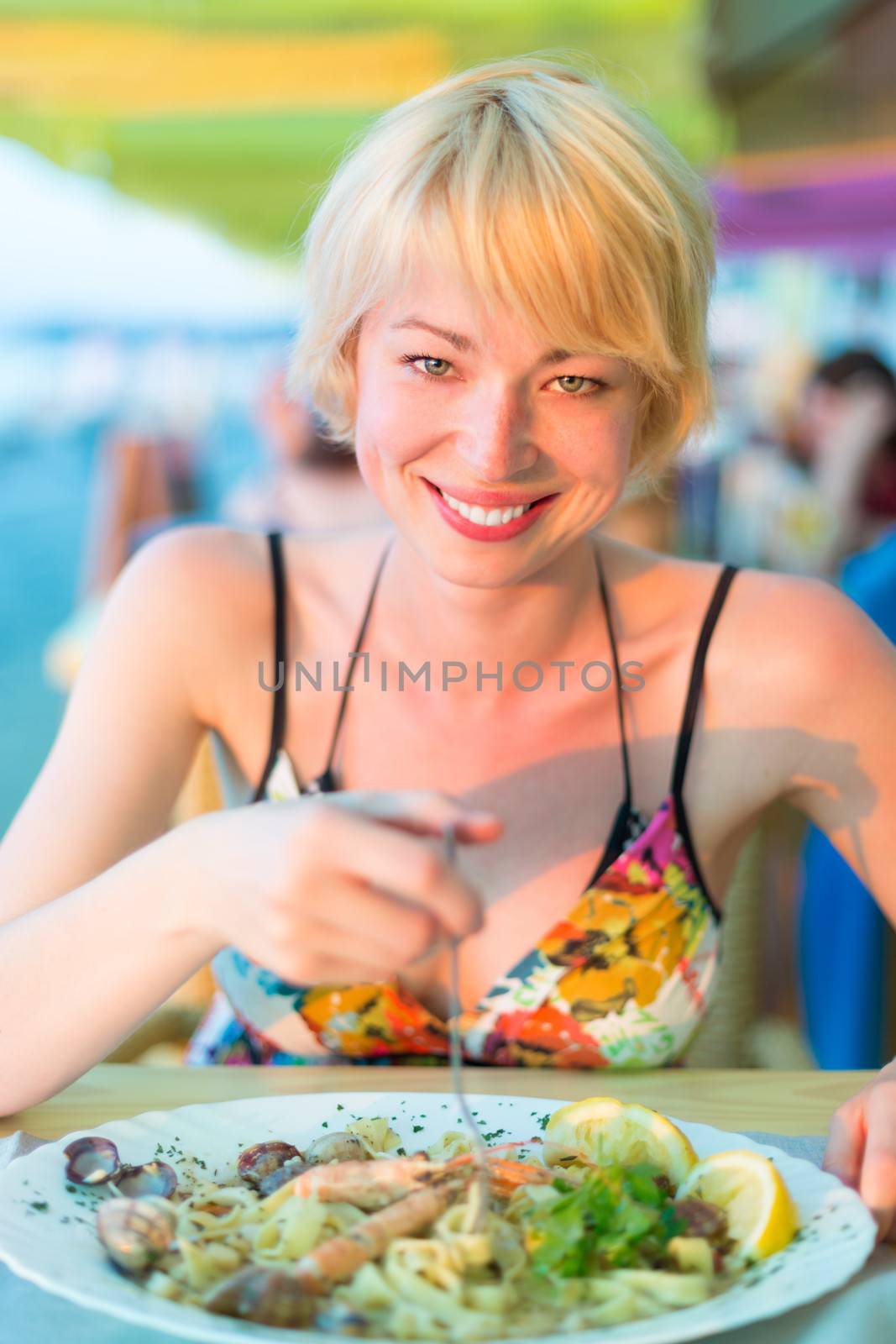 Closeup of a cheerful young woman eating healthy mediterranean sea food meal on the outdoor restaurant terrace.