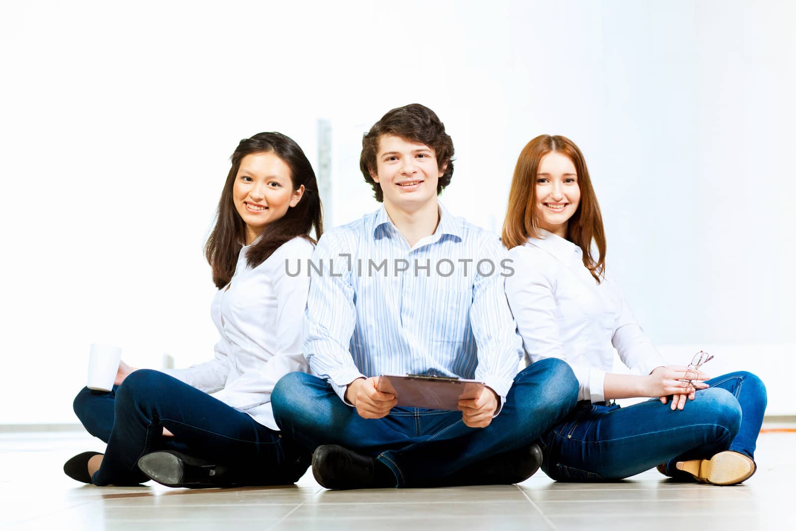 Image of three students in casual wear sitting on floor and smiling