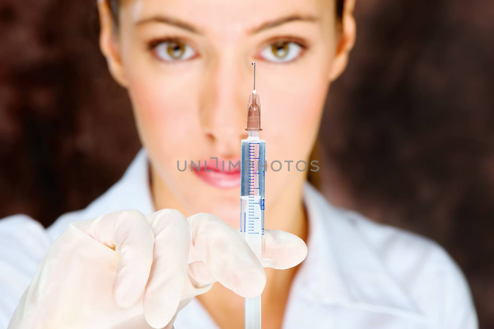 Handsome female nurse holding syringe and looking at a drop on the top of the needle reflecting reverse image of her. 