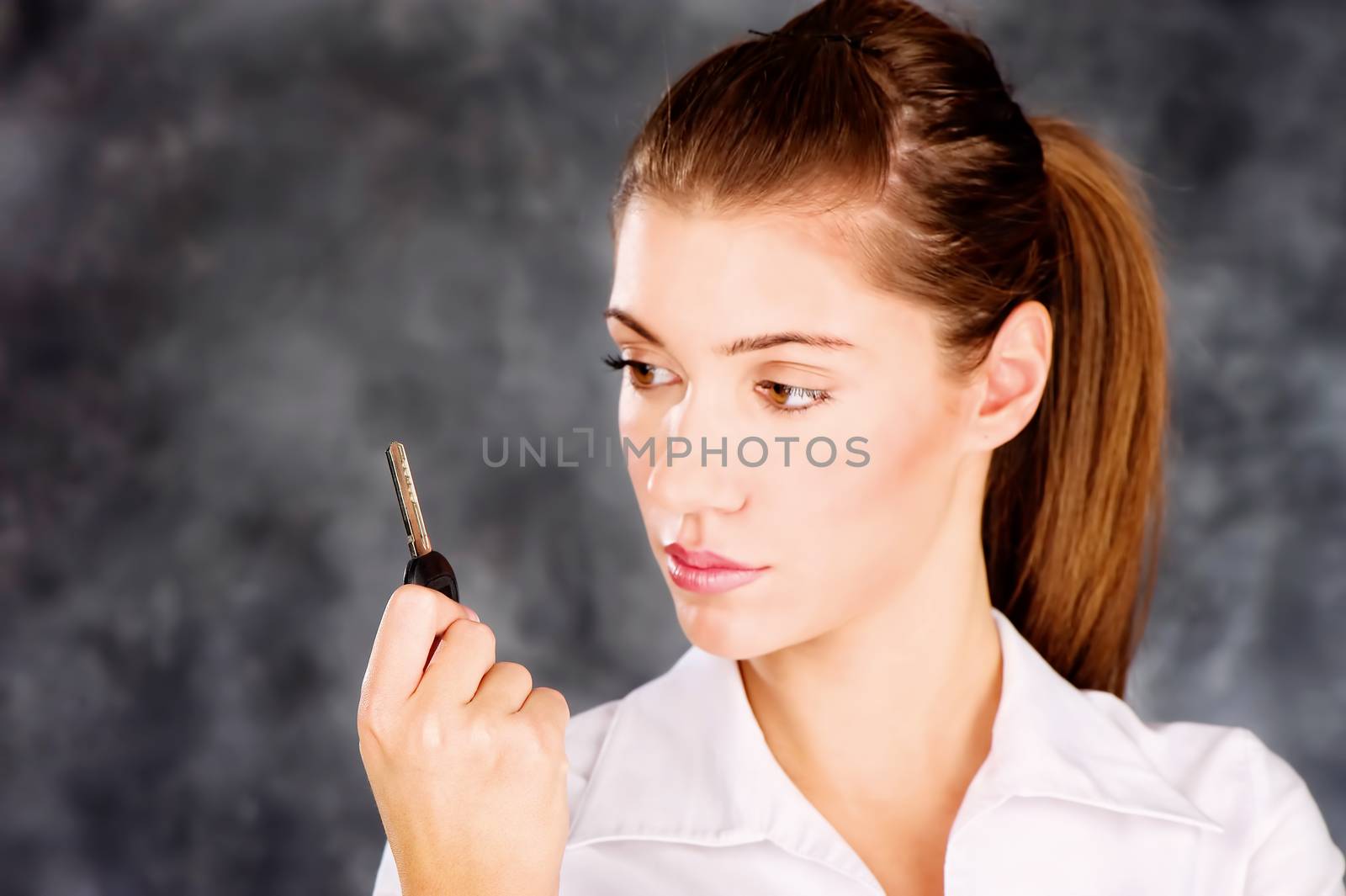 Pretty brown eye brunette looking at a key in her right hand, wearing white blouse. Focus on key