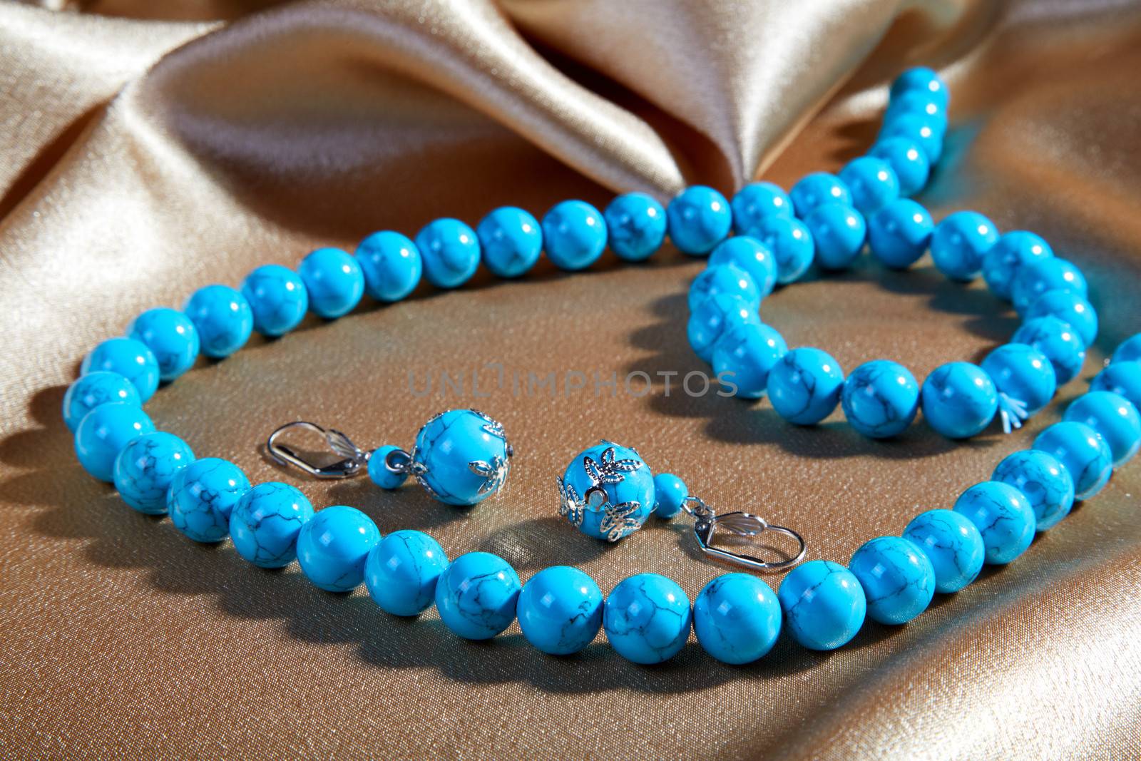 Blue necklace and earrings on a brown fabric