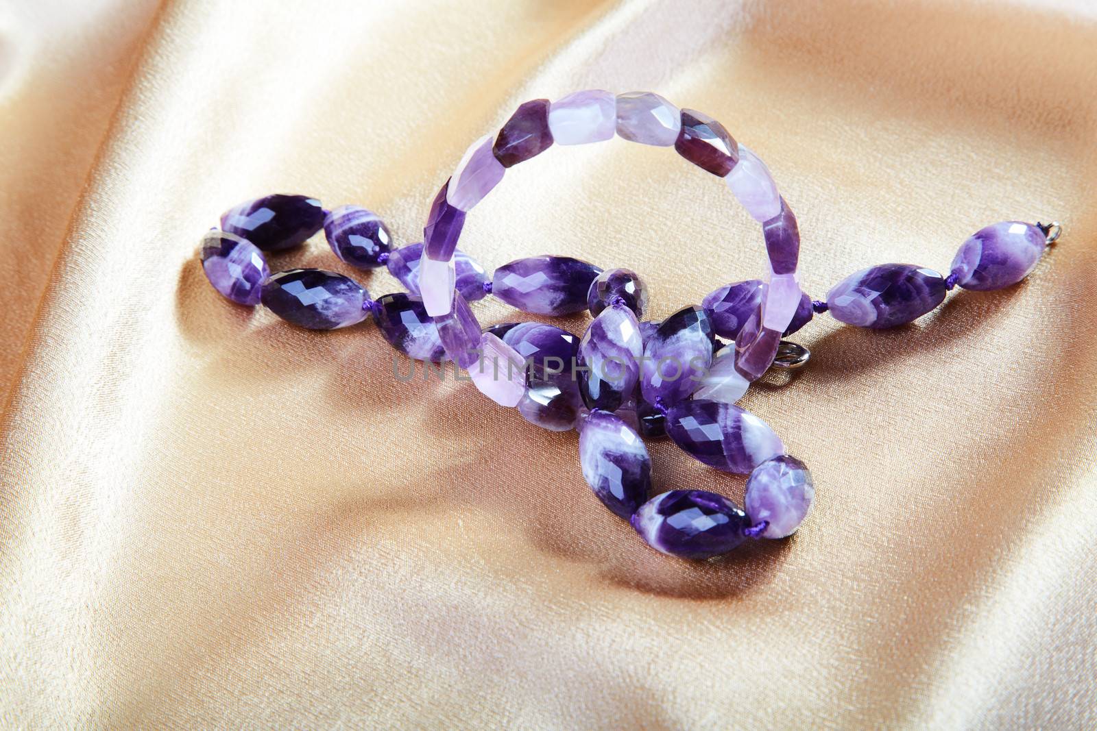 Beads and bracelet from violet glass against from a fabric
