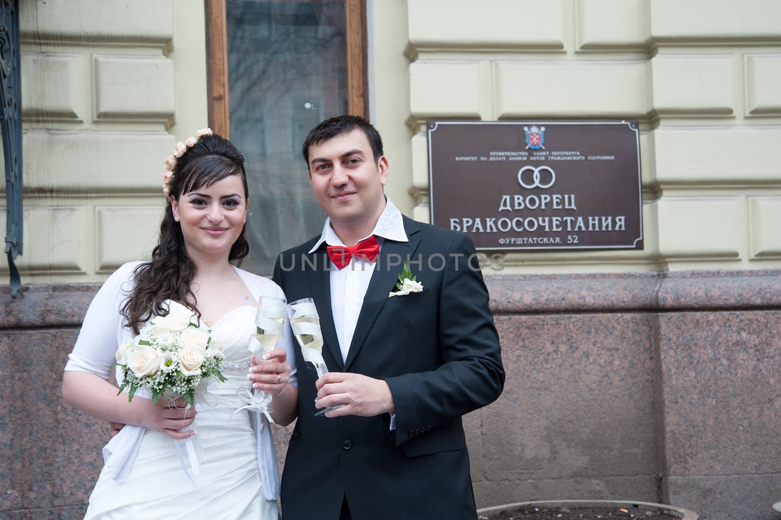 bride and groom with glasses standing at the signs of the palace