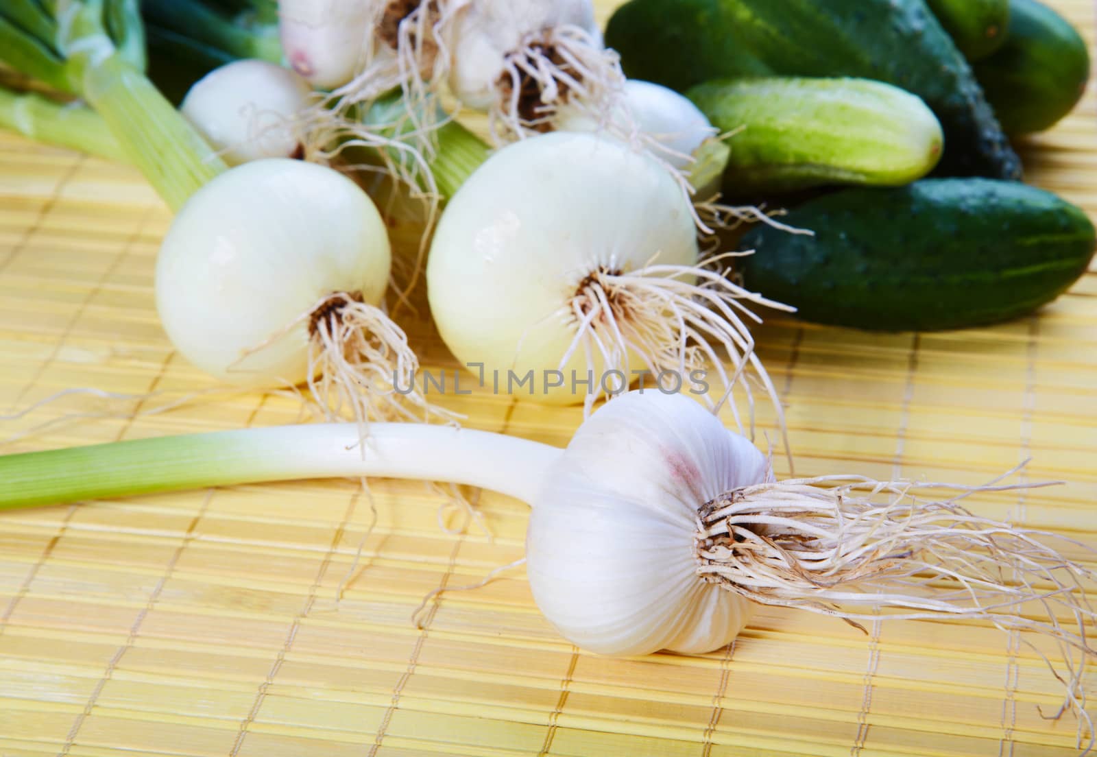 Still-life with onions garlic and green cucumbers on a table