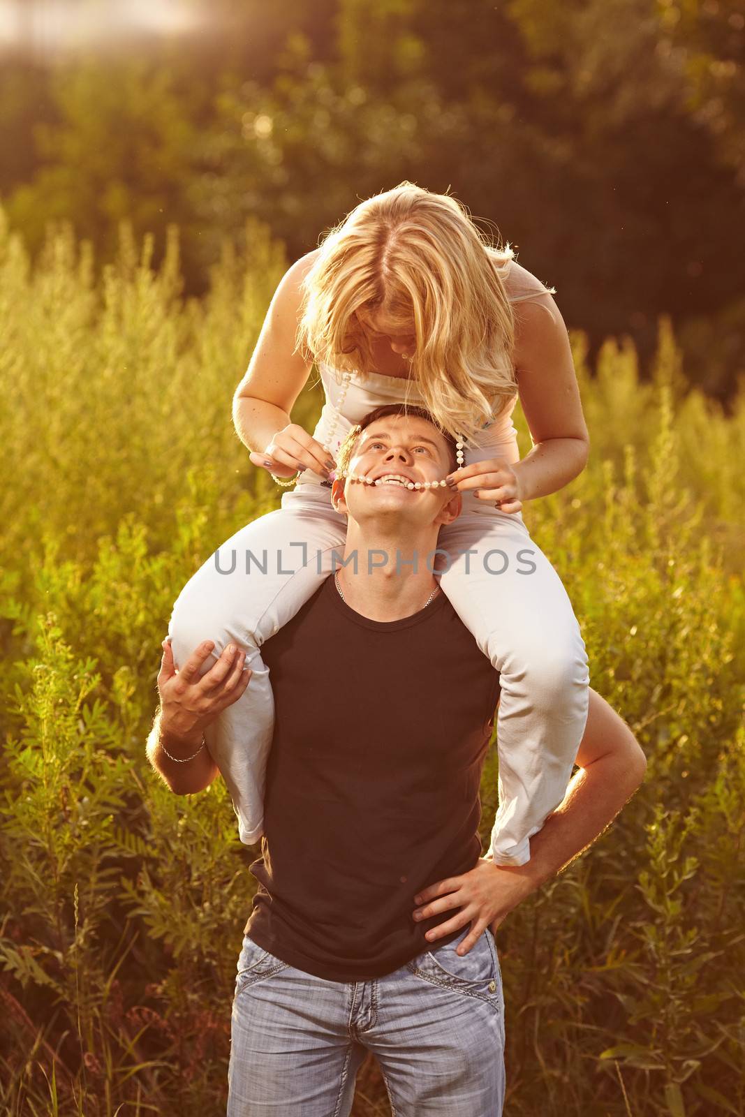Young couple on the background of the high grass. The guy holds the girl on his shoulders