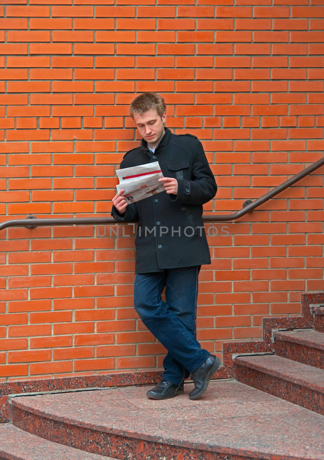 Young guy browsing news on the stairs near brick wall