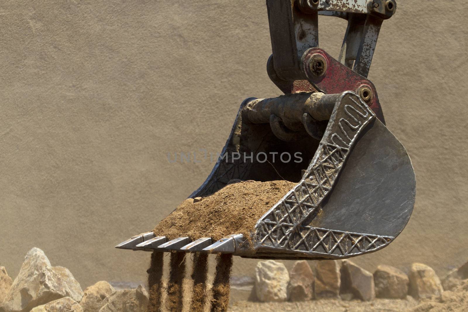 Construction machinery, a digging bucket, digs up sand, rocks, and demolishes to begin building a new, home pool and patio; copy space on stucco wall background; 