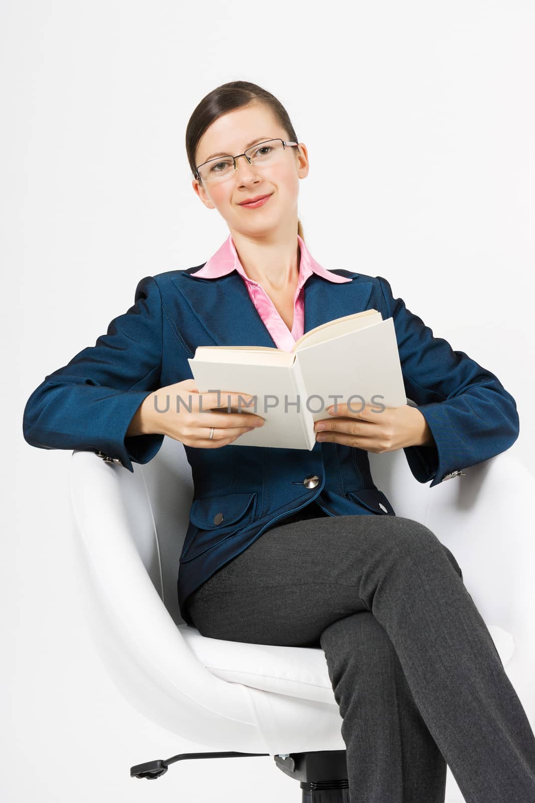 A young girl sits in a white chair with a book in hand