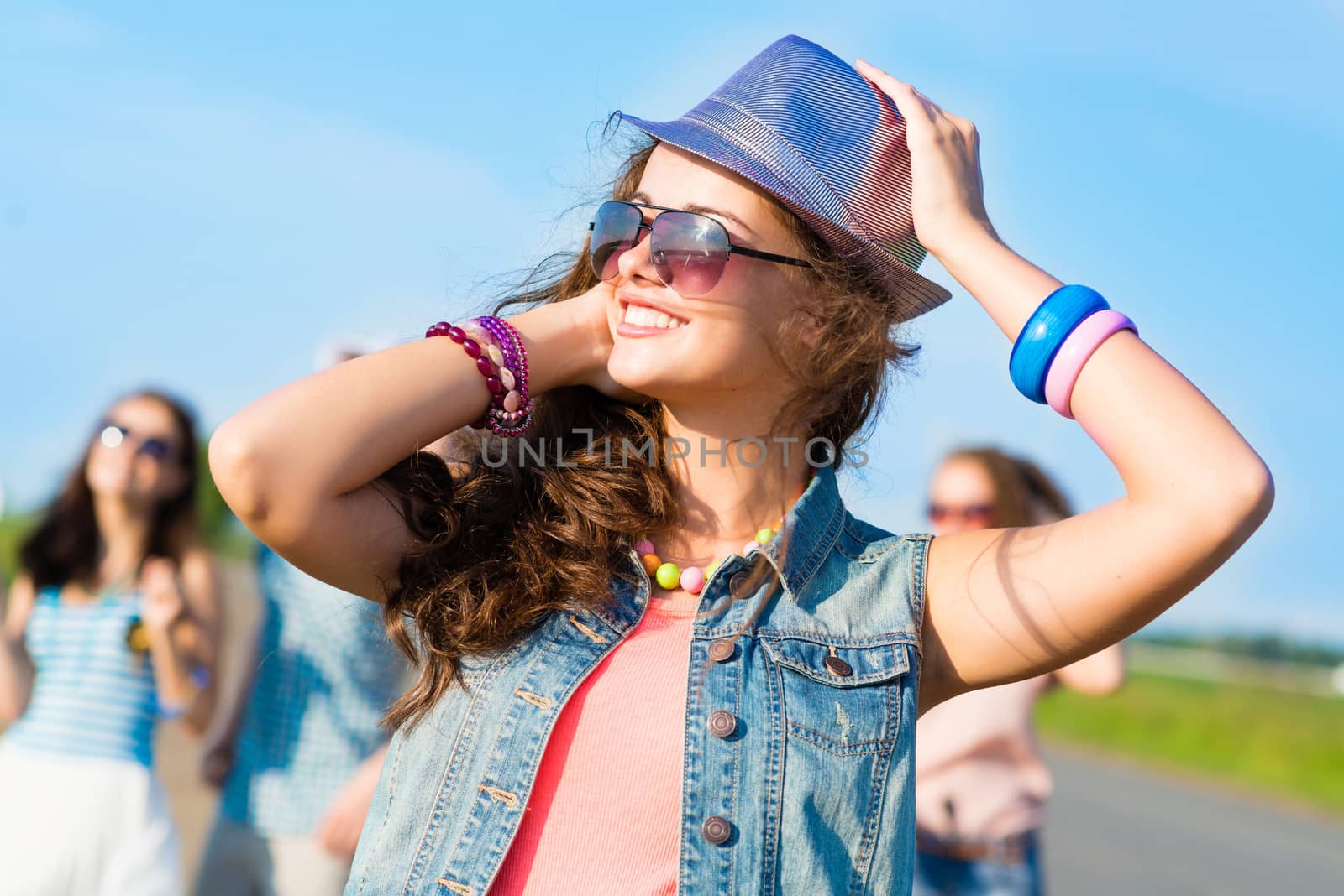 stylish young woman in sunglasses on the background of blue sky and friends