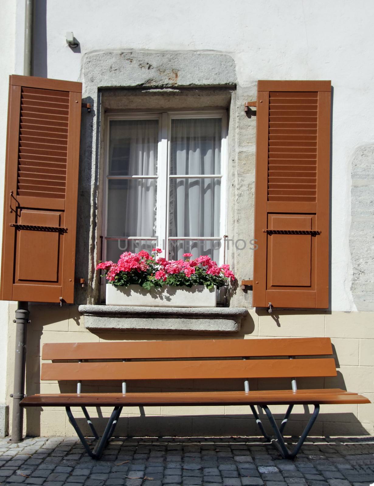 Brown bench under old window with shutters in front of white wall, Estavayer-le-lac, Switzerland