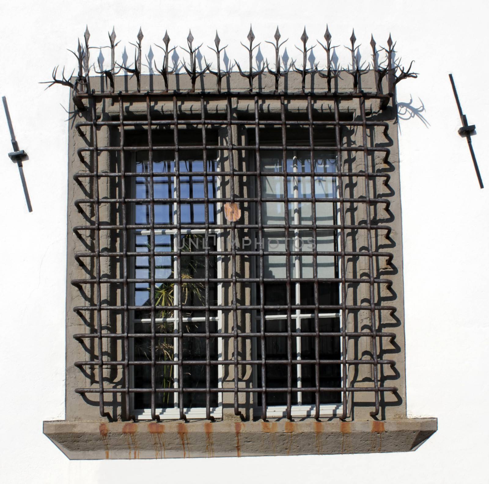 Close up of window with black iron bar grill in white wall