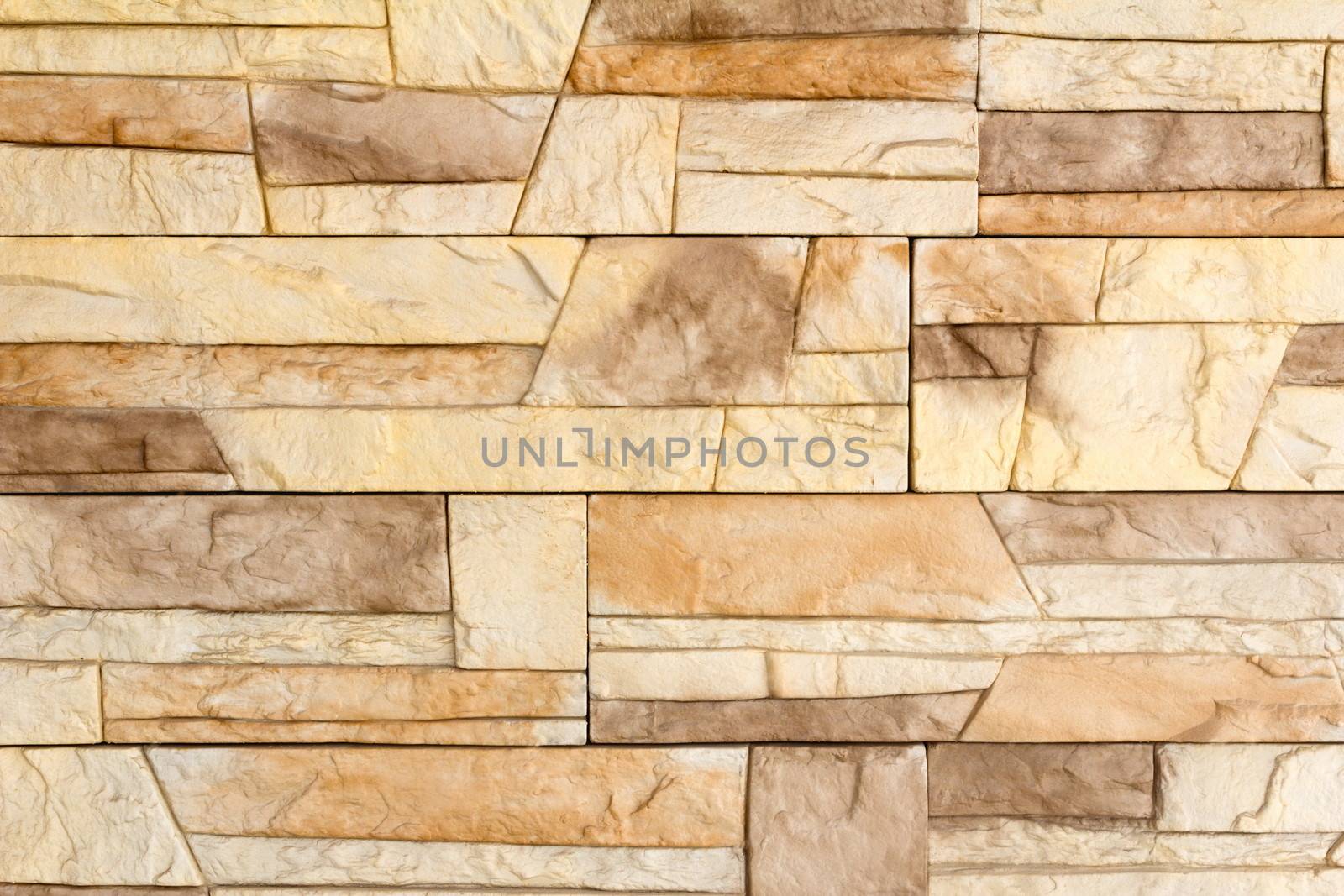 Fragment of a wall of the house covered with a light brown ceramic tile, imitating a natural stone.