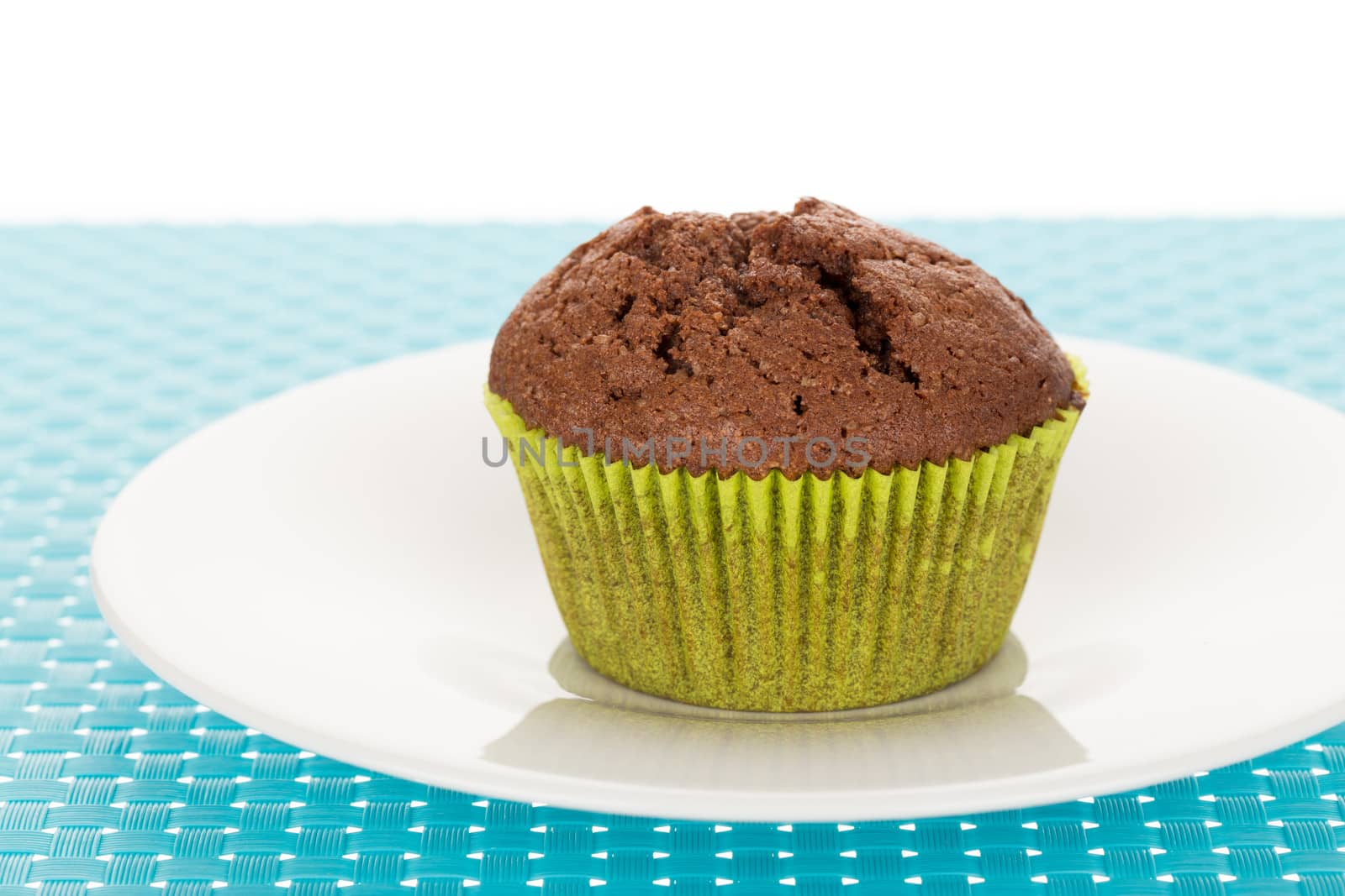 Delicious homemade chocolate muffin on white plate on blue tablemat.