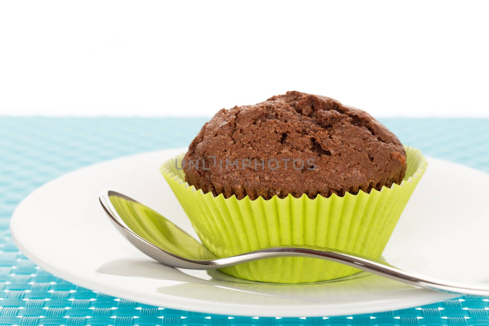 Delicious homemade chocolate muffin on white plate on blue tablemat.