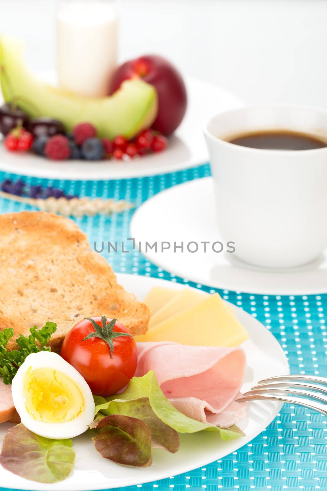 Breakfast with toast, cheese, sausage, ham, tomato, egg, cup of coffee and plate of fruits.