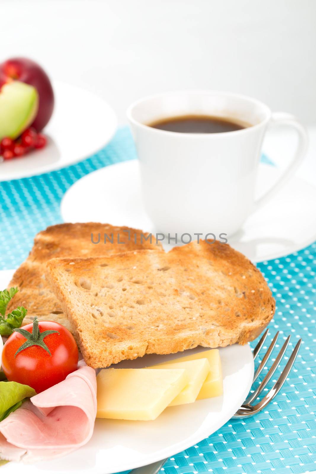 Breakfast with toast, cheese, sausage, ham, tomato, egg, cup of coffee and plate of fruits.