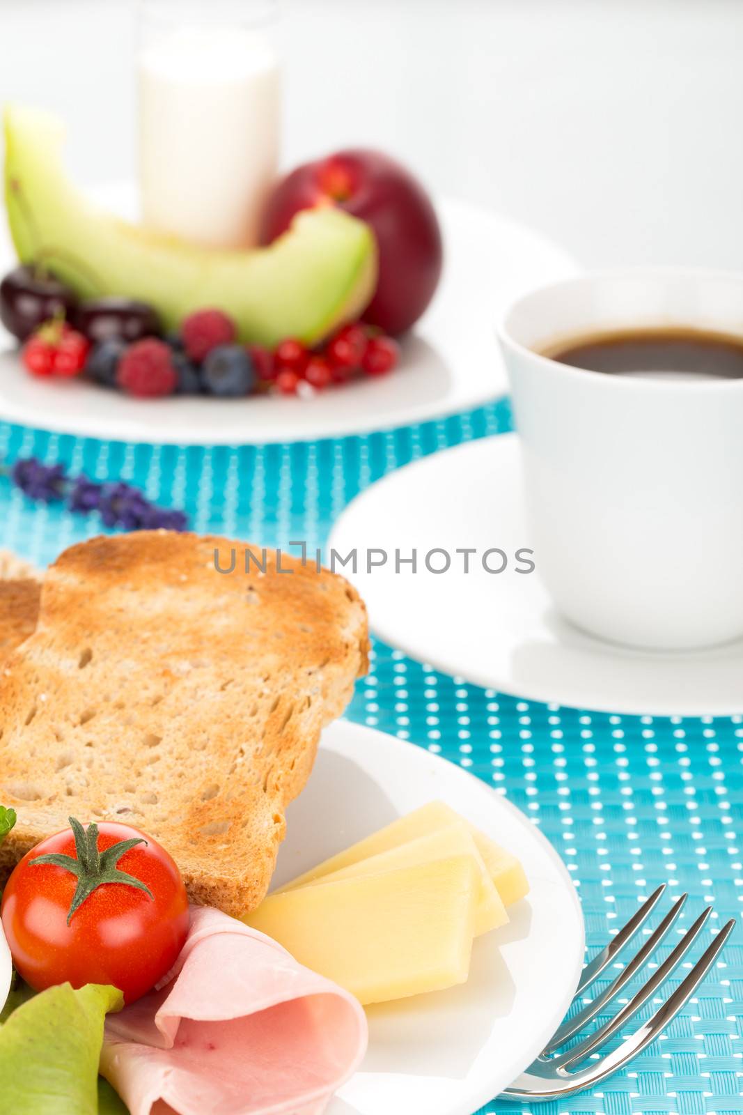 Breakfast with toast, cheese, sausage, ham, tomato, egg, cup of coffee and plate of fruits.