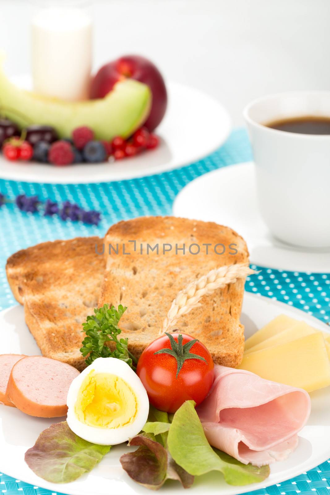 Breakfast with toast, cheese, sausage, ham, tomato, egg, cup of coffee and plate of fruits.