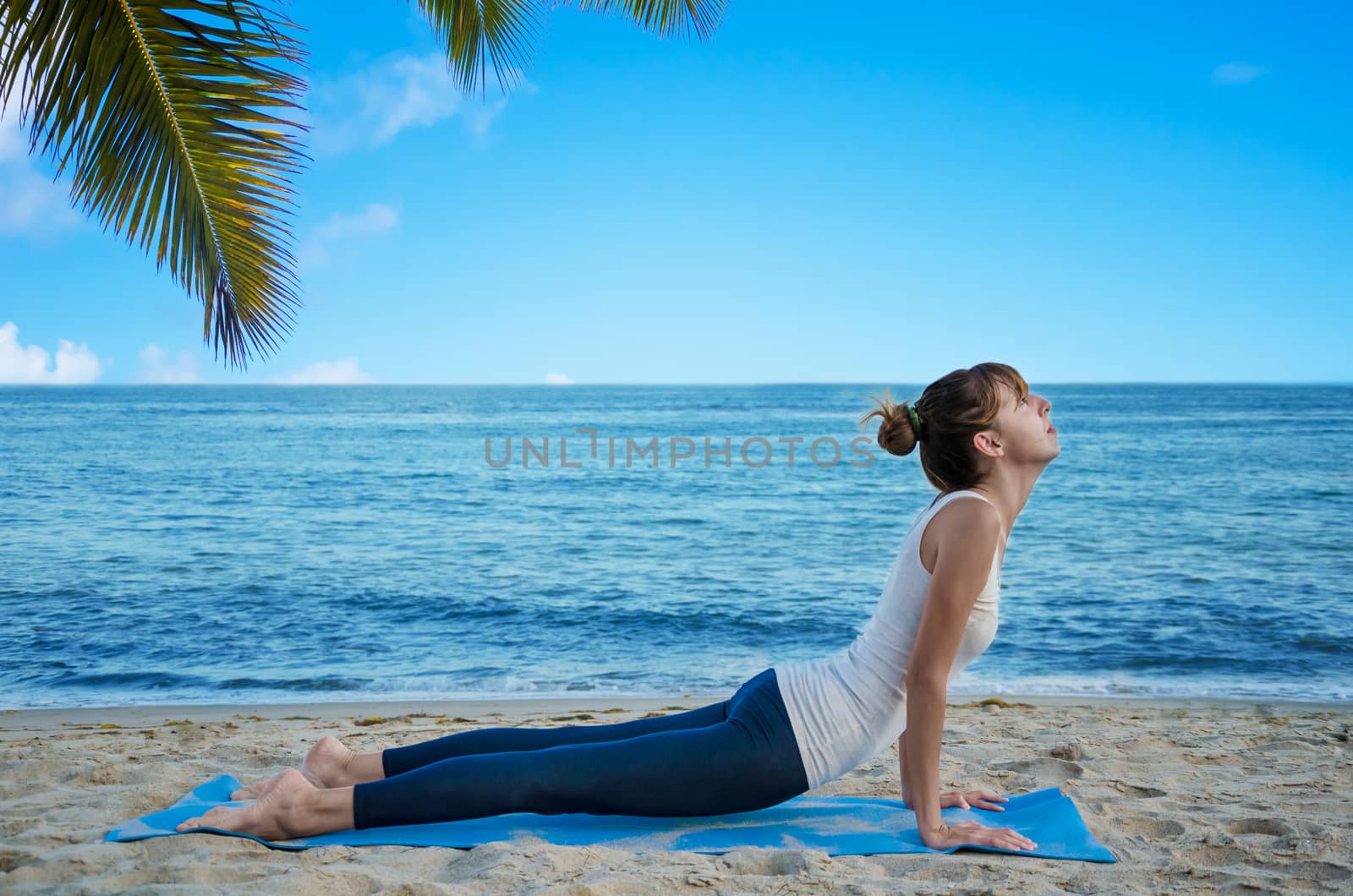 Young pretty woman practicing yoga on the beach by the ocean 