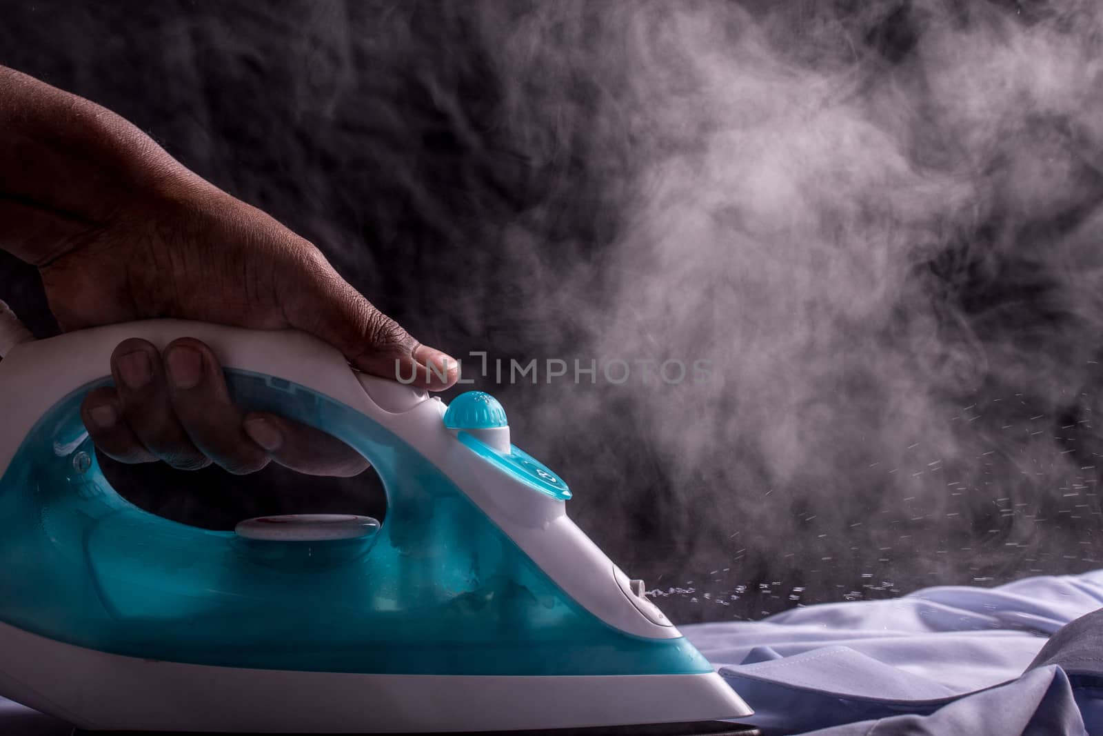 A person ironing a shirt with a steaming hot electric iron