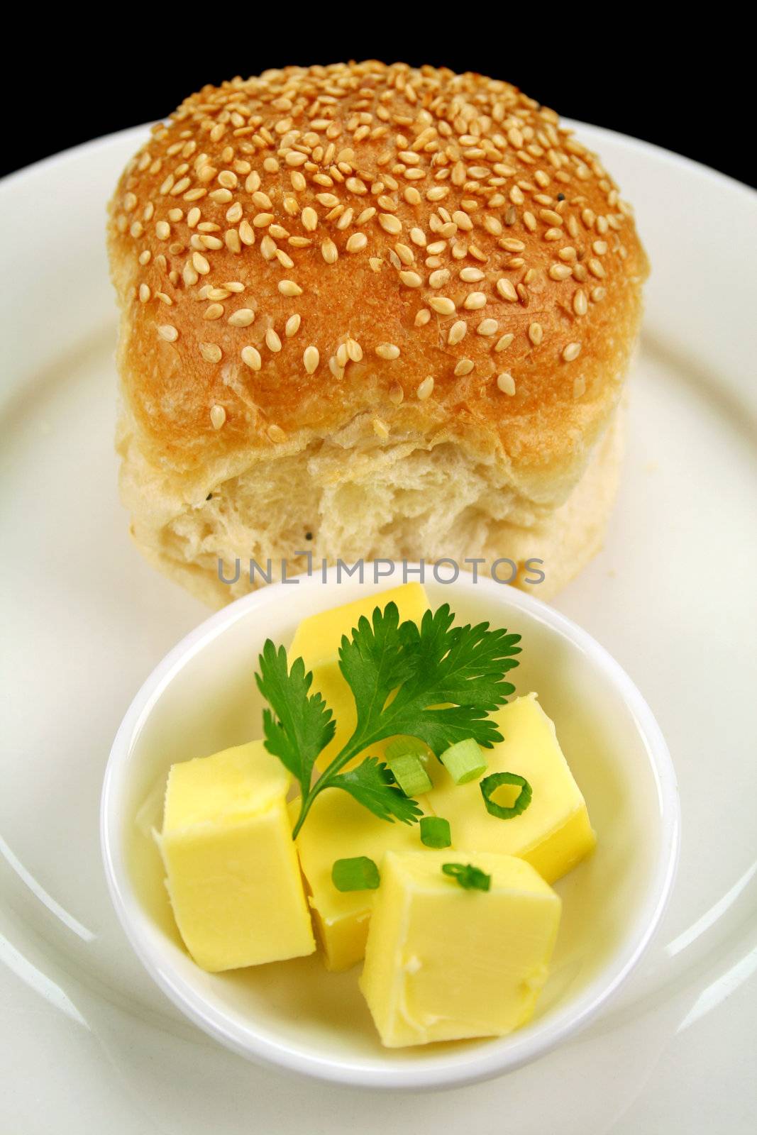 Dinner bread roll with dish of butter with green garnish.