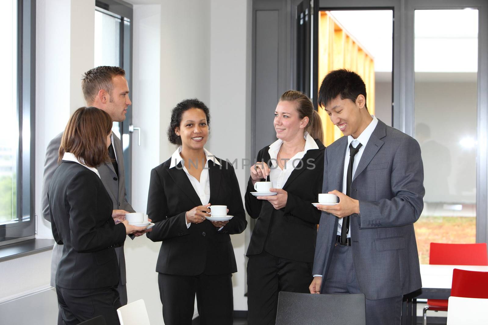 Group of diverse multiethnic businesspeople on coffee break with three ladies and two men standing together chatting in smart suits