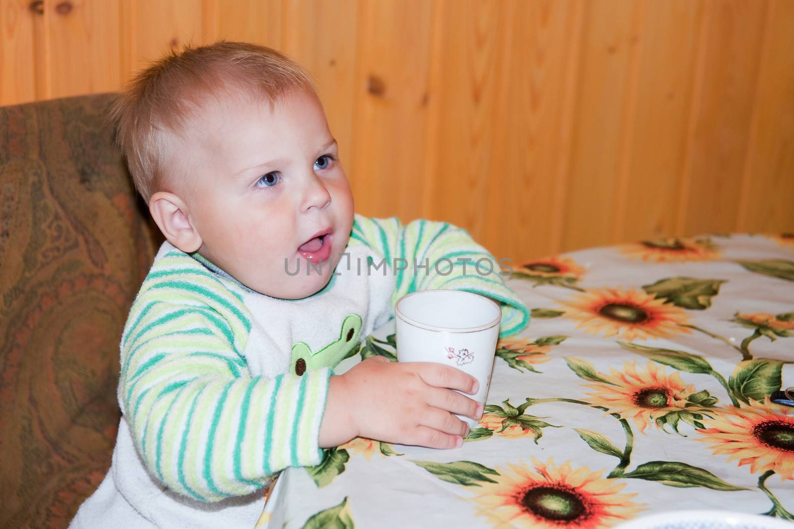 little boy is drinking at a table in the kitchen