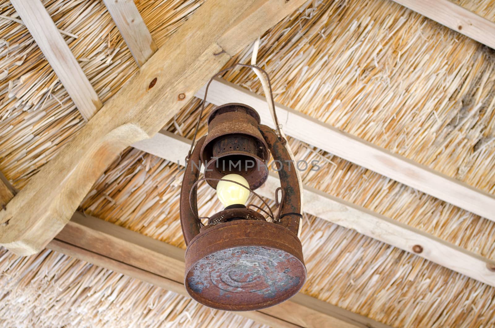 old rusty metal lamp hang on bower straw roof ceiling with electric bulb.