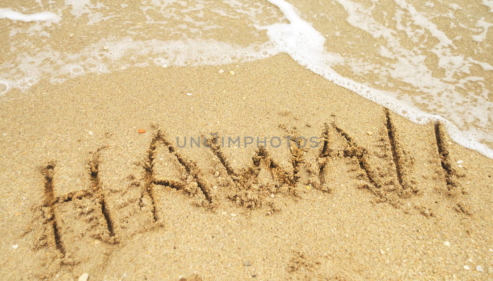 A warm tropical beach and Hawaii written in the sand 